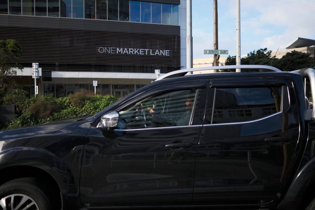 A black vehicle parked in front of a modern building with the sign 'One Market Lane'.
