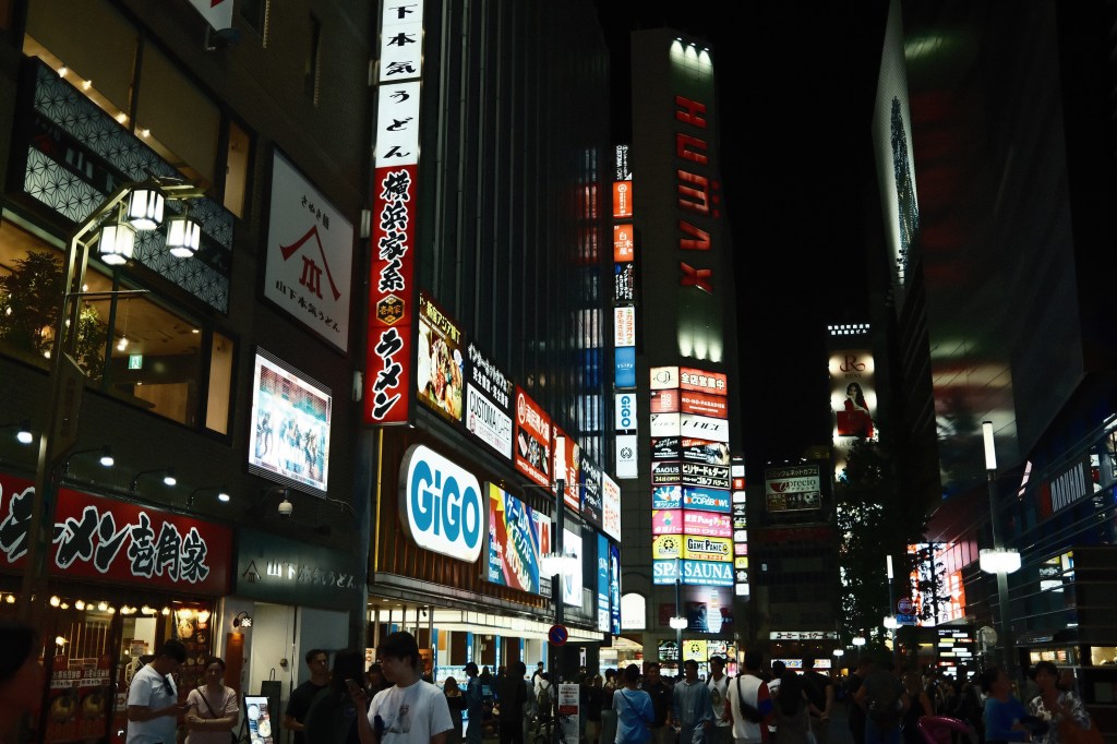 A busy urban street at night filled with colorful neon signs and storefronts in a bustling area.