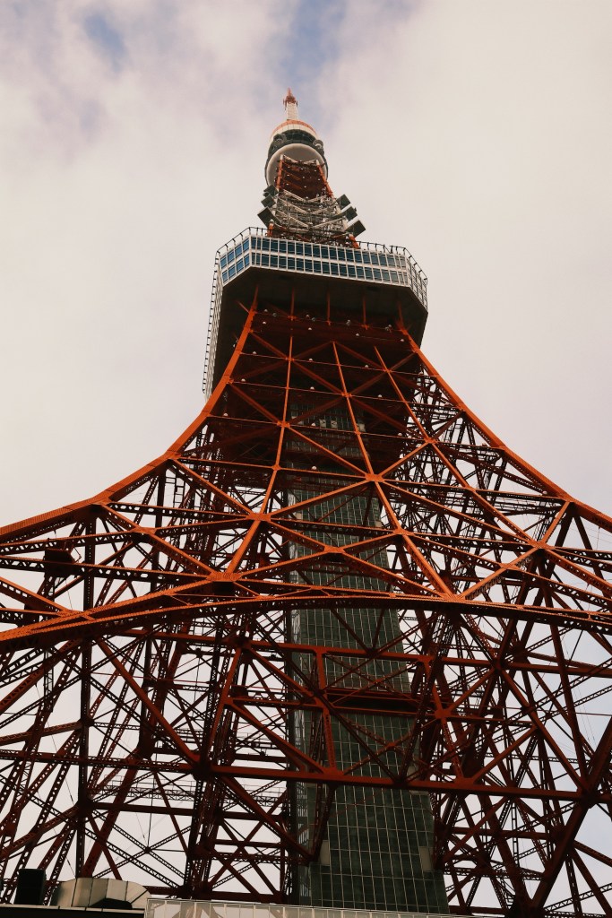 View of Tokyo Tower from below, showcasing its red and white structure against a cloudy sky.