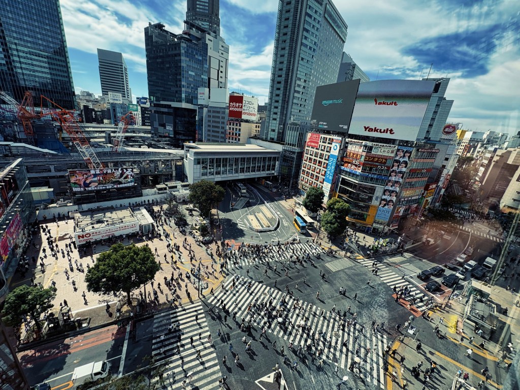 Aerial view of a busy urban intersection with pedestrians crossing and city buildings in the background.
