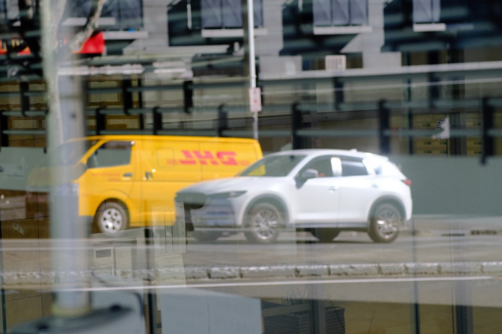 Reflection of a yellow delivery van and a white SUV parked on the street.