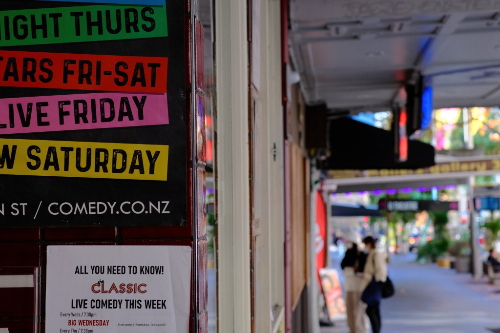 A vibrant sign advertising live comedy events at a venue, featuring schedules for performances on Thursday, Friday, and Saturday, as well as a flyer for Wednesday comedy shows.