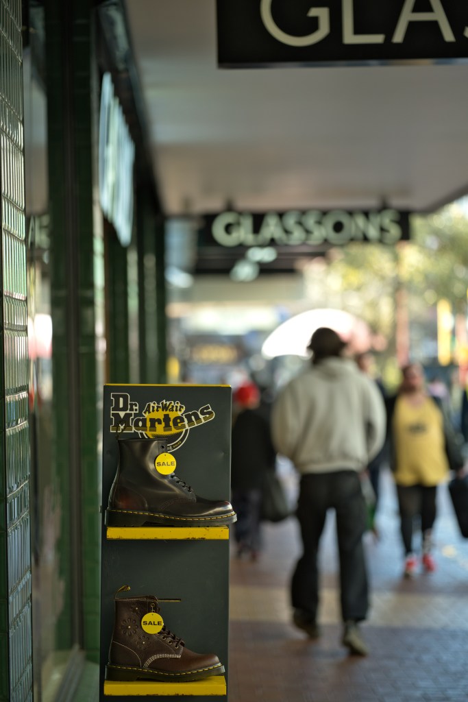 Display of Dr. Martens boots on sale outside a retail store, with shoppers walking in the background.
