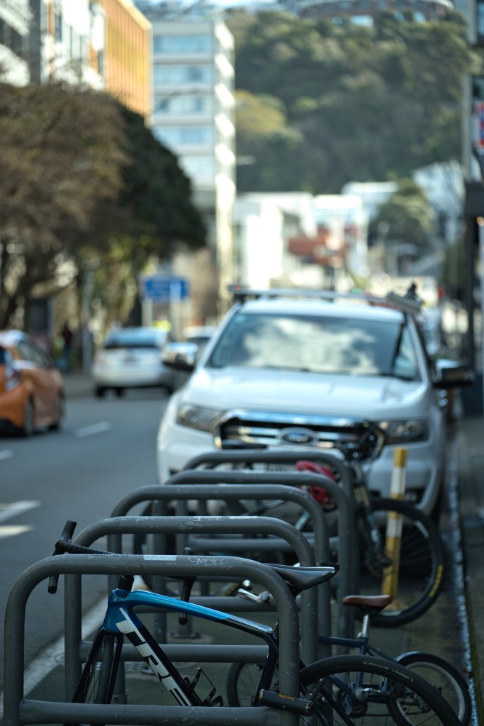 Bicycles parked in a bike rack on a city street with cars and buildings in the background.