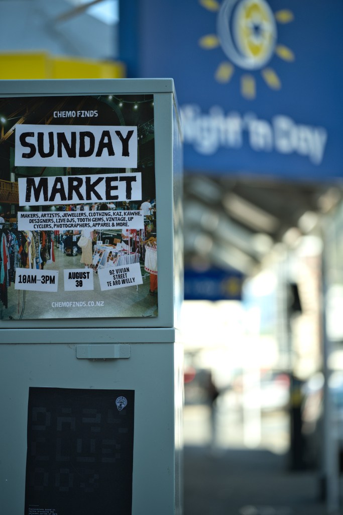 A notice for the 'Sunday Market' event featuring details such as makers, artists, and live DJs, displayed on a street post with a blurred background of a sunny day.