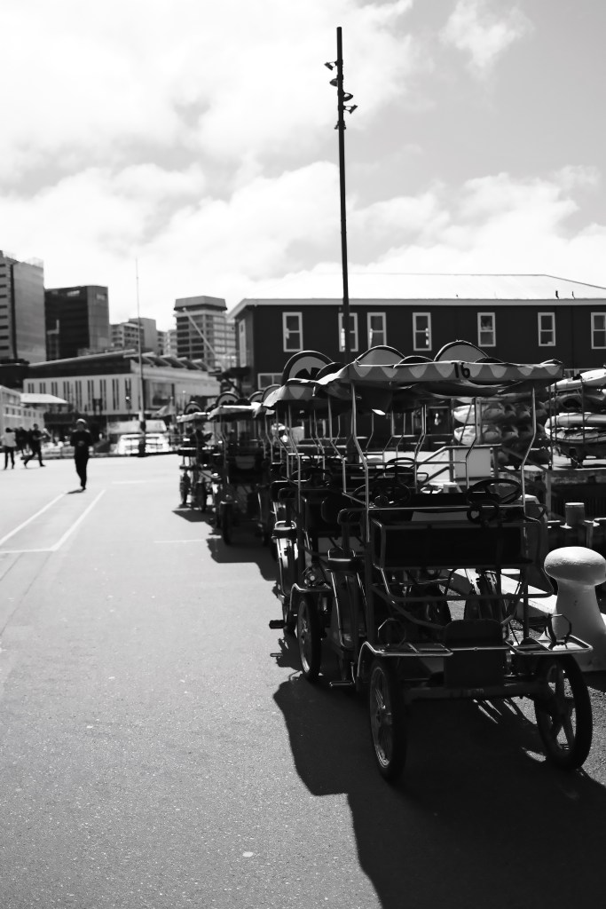 Row of parked pedal carts along a city street under a cloudy sky.